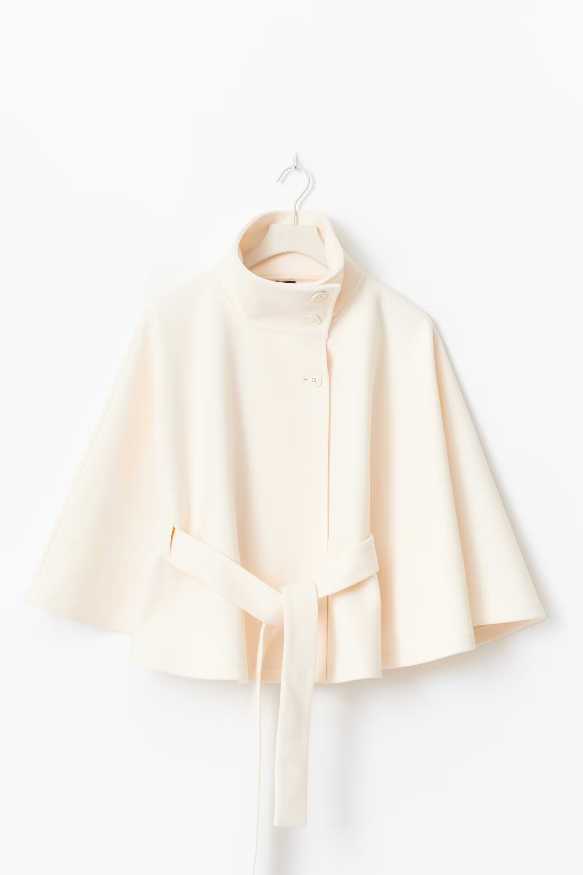 Creme kleurige cape jas met hoge kraag en knoopsluiting – close-up voorkant